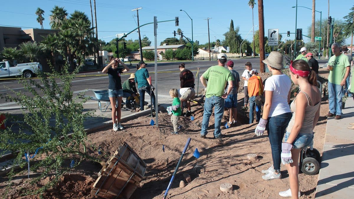 Volunteers with shovels and a wheelbarrow digging up a strip of ground beside a city sidewalk