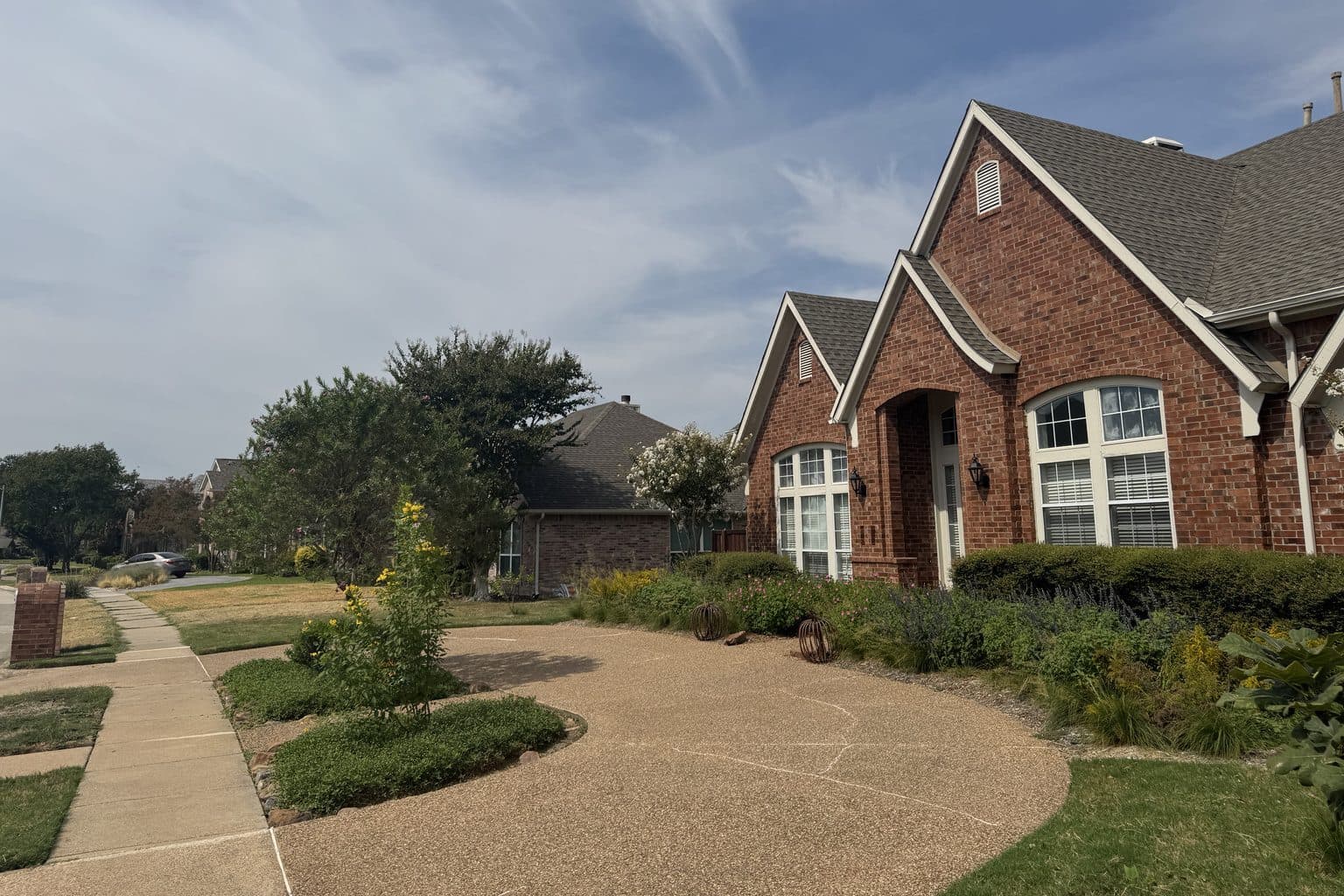 A brick house with a curved aggregate drive, island beds of frogfruit and a foundation bed of goldenrod, salvia and grasses