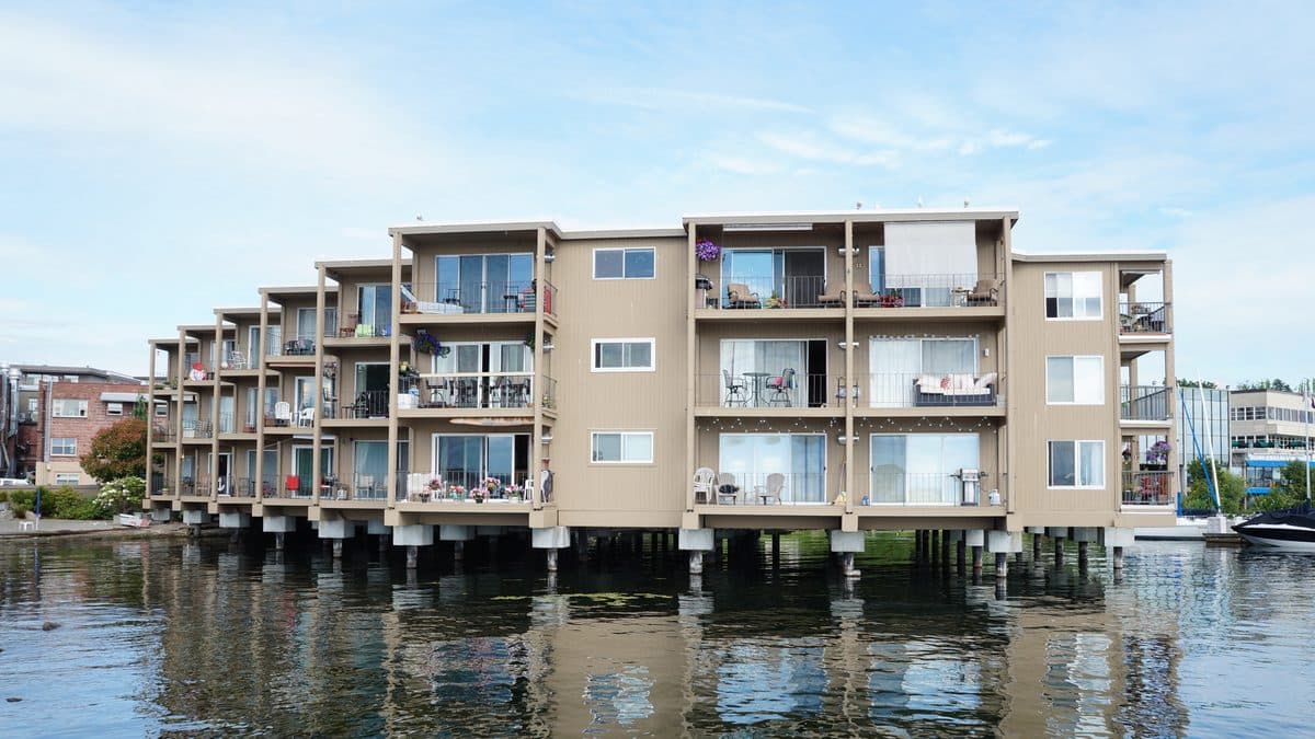 A four-story condominium building with balconies standing over the water