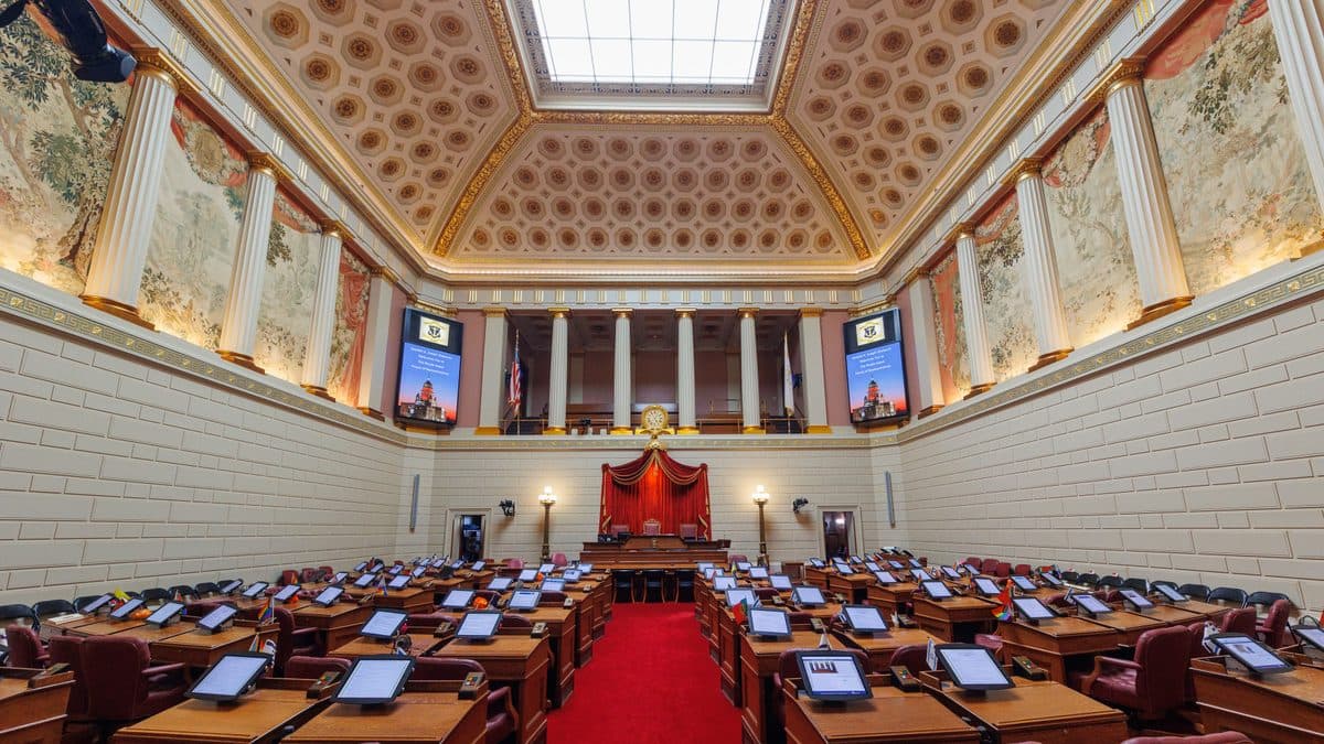 The empty House chamber in the Rhode Island State House, with rows of desks and a red carpet