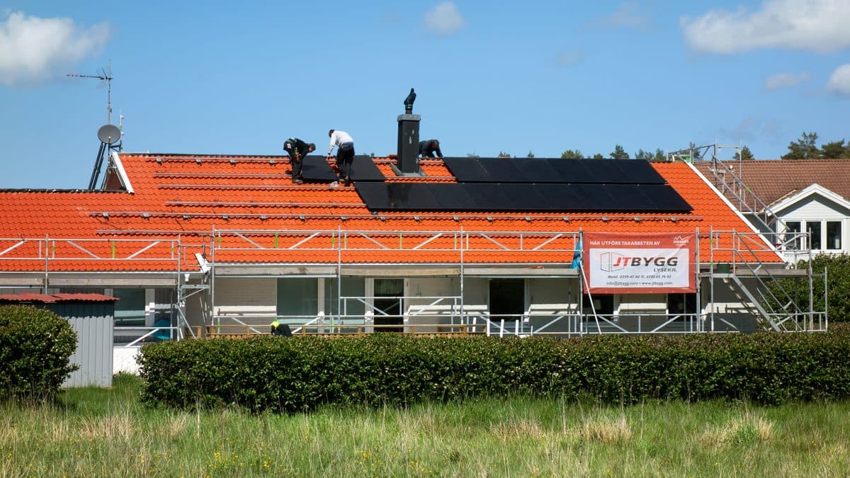 Workers installing solar panels on the tile roof of a house surrounded by scaffolding